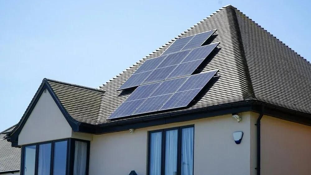 Sonnenbeschienenes Haus mit Solarmodule am Dach vor blauem Himmel