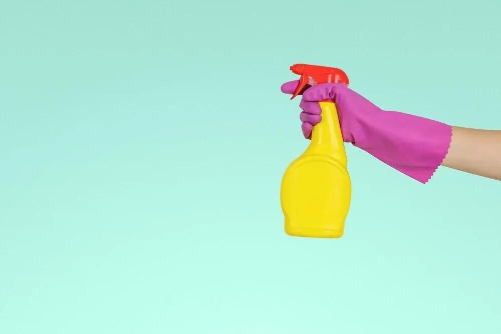 Flasche mit Reiniungsmittel in einer Hand mit Putzhandschuh