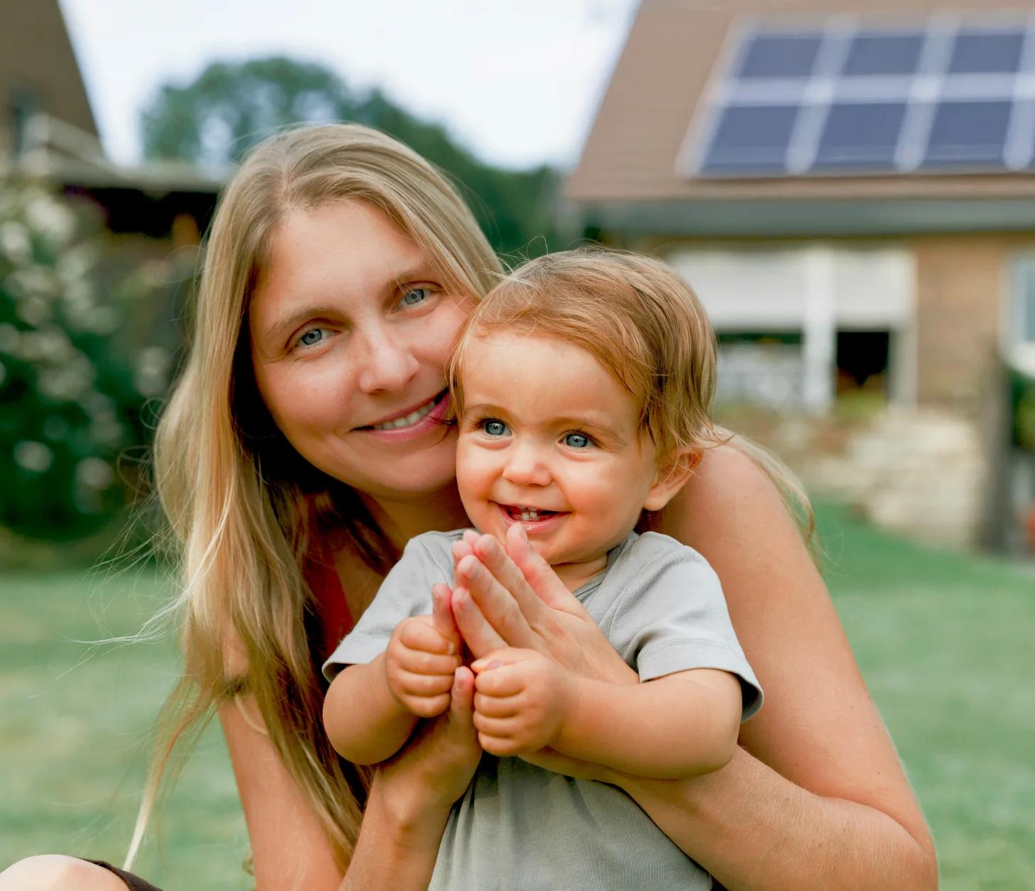 Mutter und Kind mit einem Haus mit Photovoltaik im Hintergrund